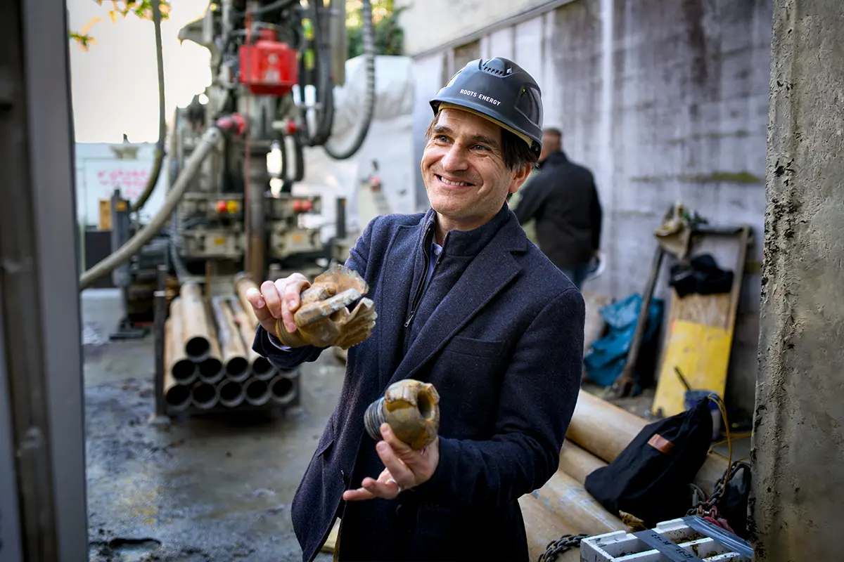 Person mit Roots-Energy-Helm hält Bohrkronen vor der Bohranlage